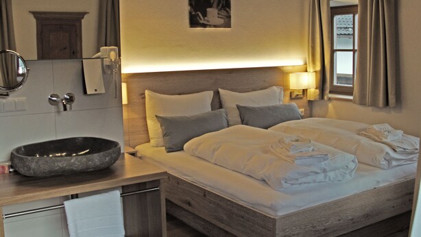 A hotel room with a wooden bed, a round sink, a mirror, and a framed picture on the wall. - Mammhofer Suite & Breakfast (Oberammergau)