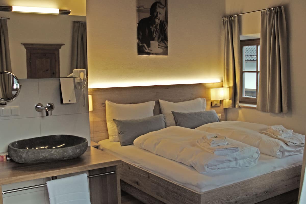 A hotel room with a wooden bed, a round sink, a mirror, and a framed picture on the wall.