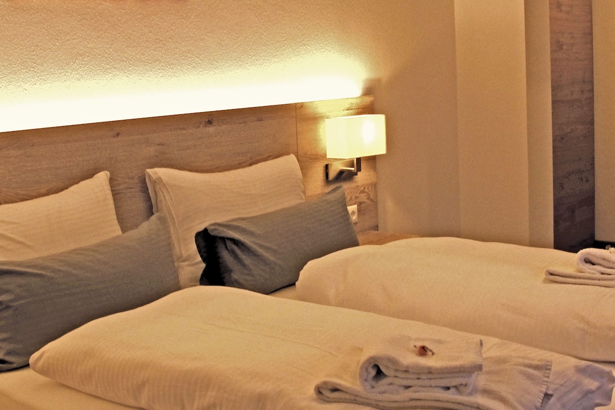 A hotel room with two beds, a nightstand with a lamp, and a painting on the wall.