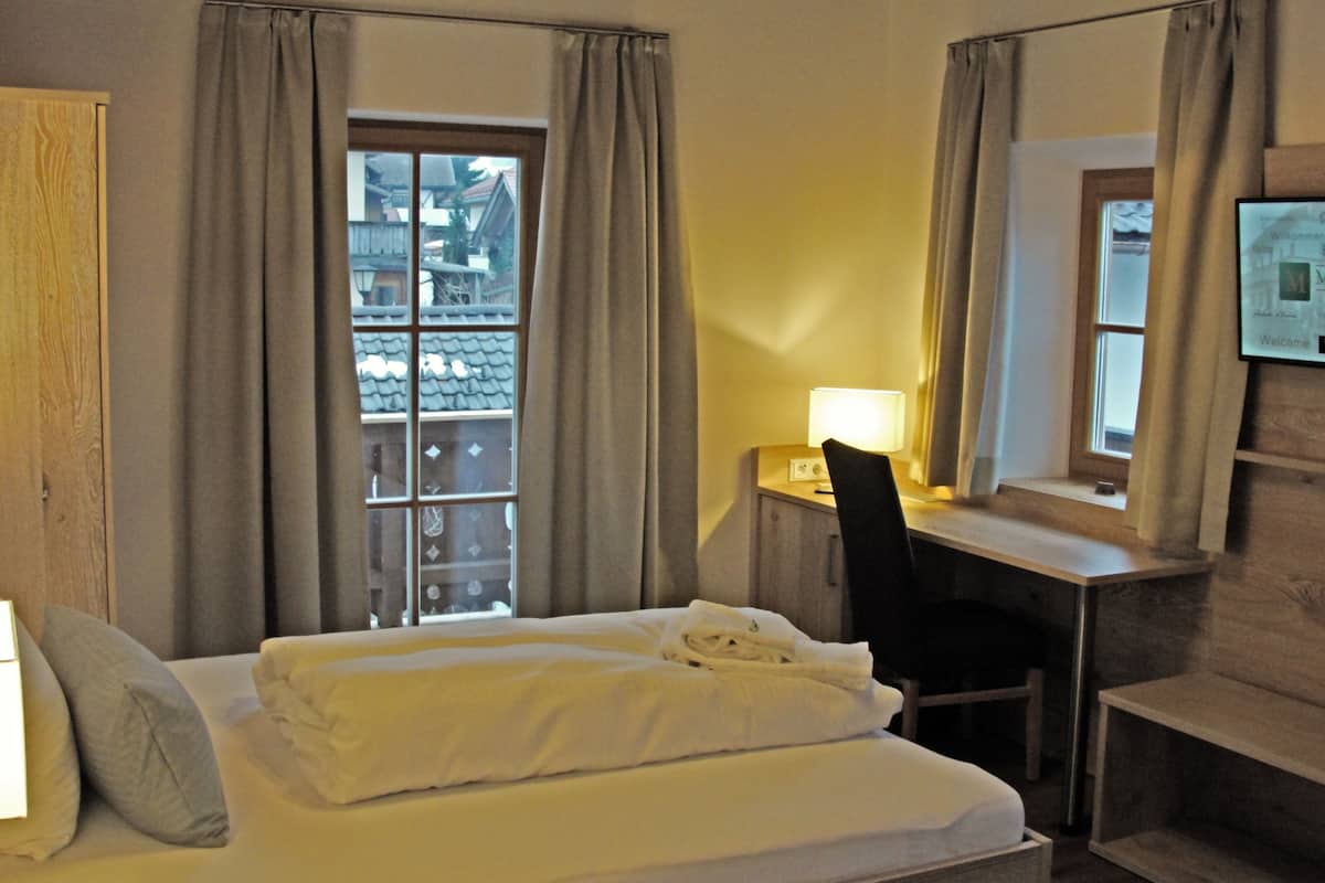 A hotel room with a bed, a desk, a chair, and a window with curtains.