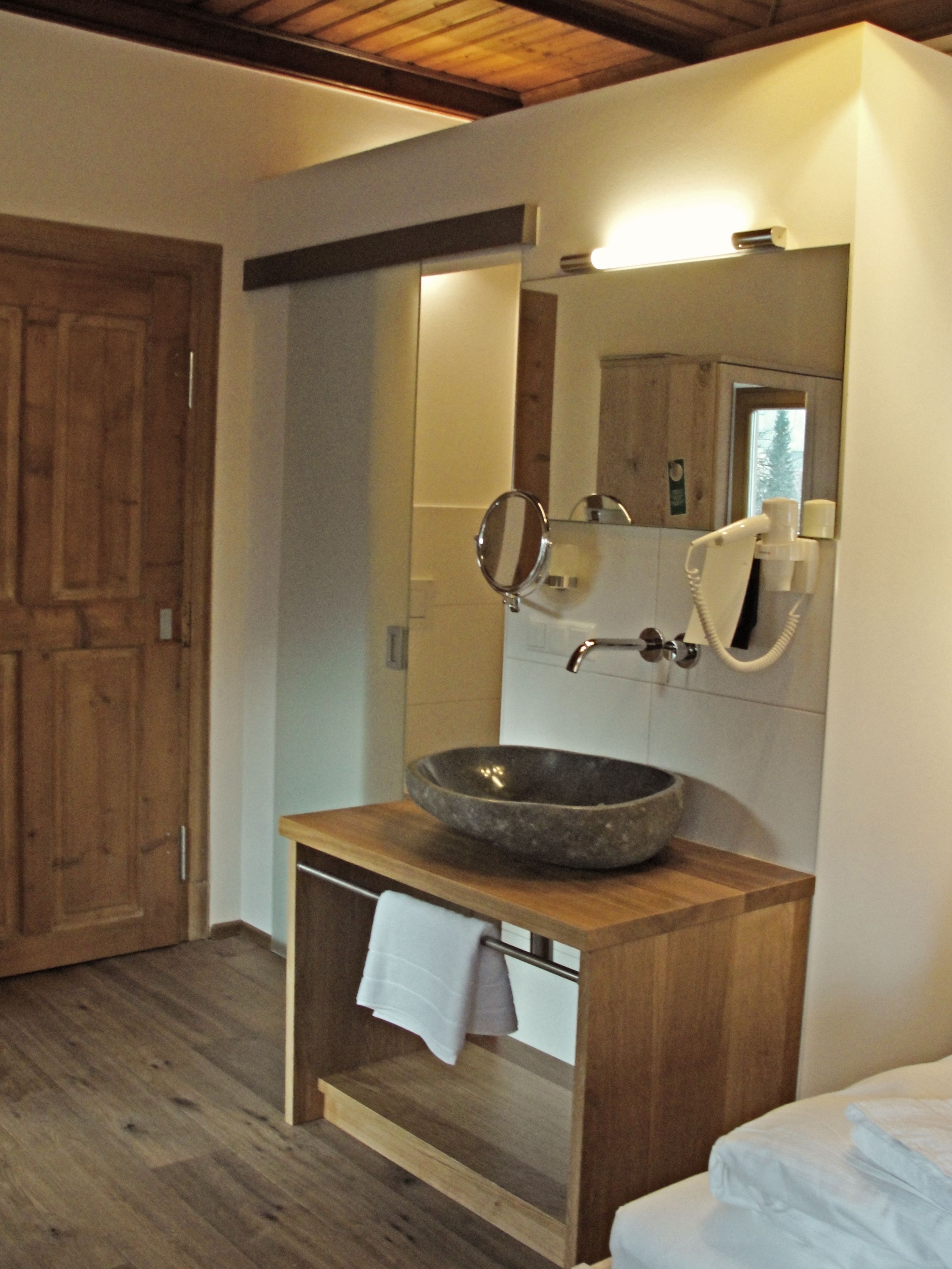 A bathroom with a wooden vanity, a large mirror, a stone basin, and a towel hanging on the wall.