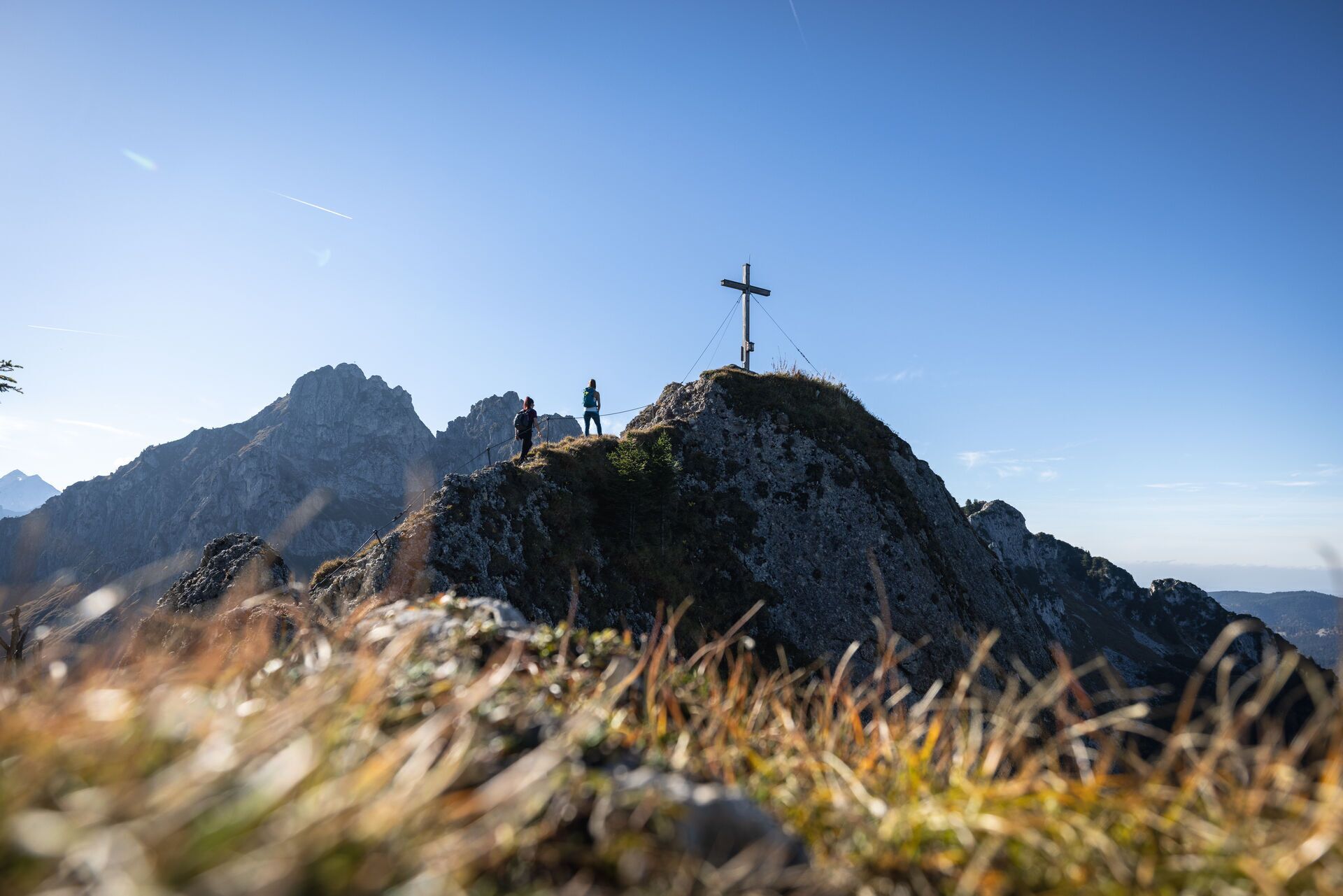 Ein Berggipfel mit einem Kreuz, felsiges Gelände und entfernte Berge.