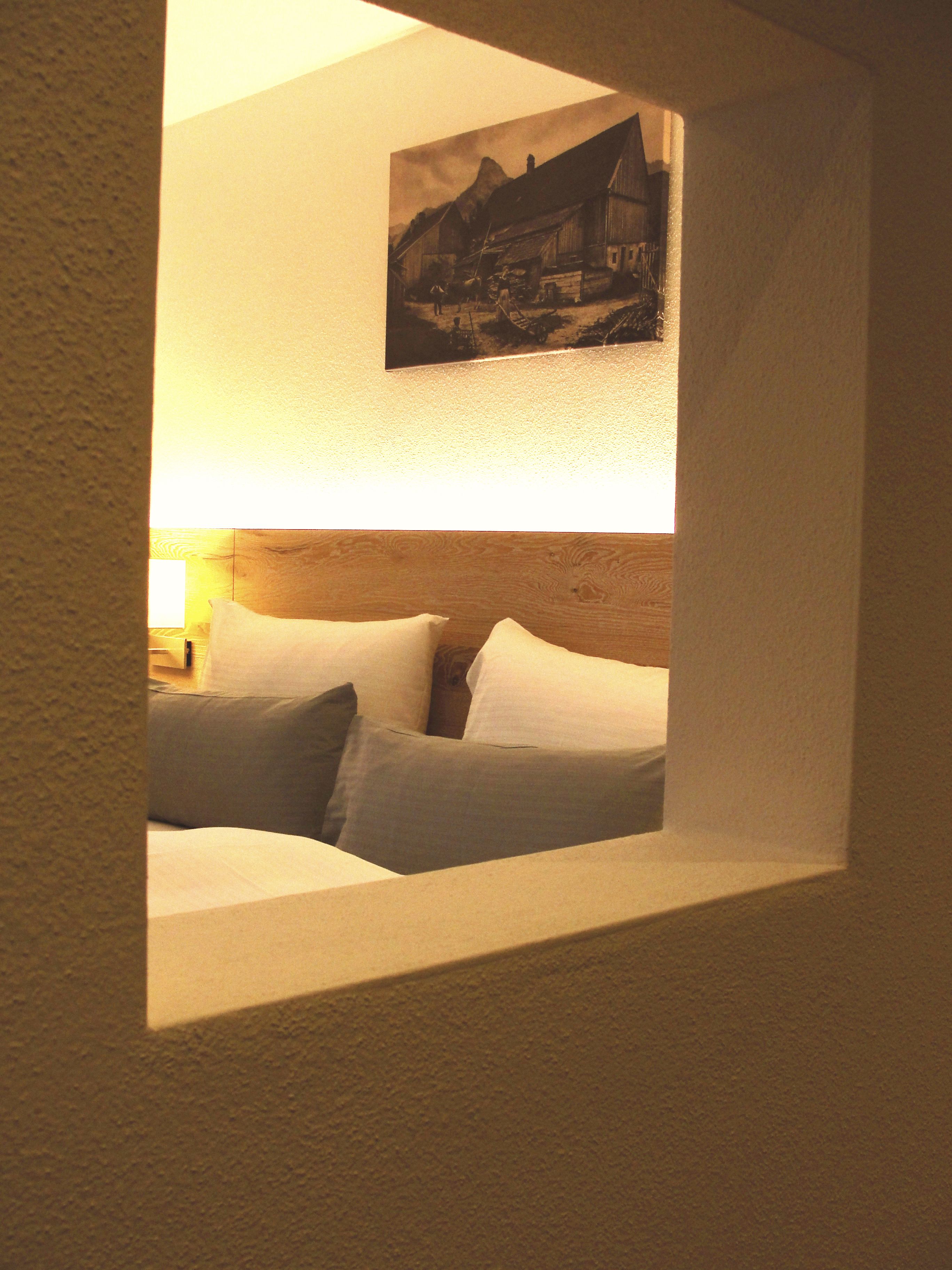 Een slaapkamer met een bed, kussens, een nachtkastje en een aan de muur hangend schilderij.