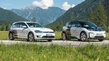 Two white electric cars parked on a road with a mountainous backdrop.