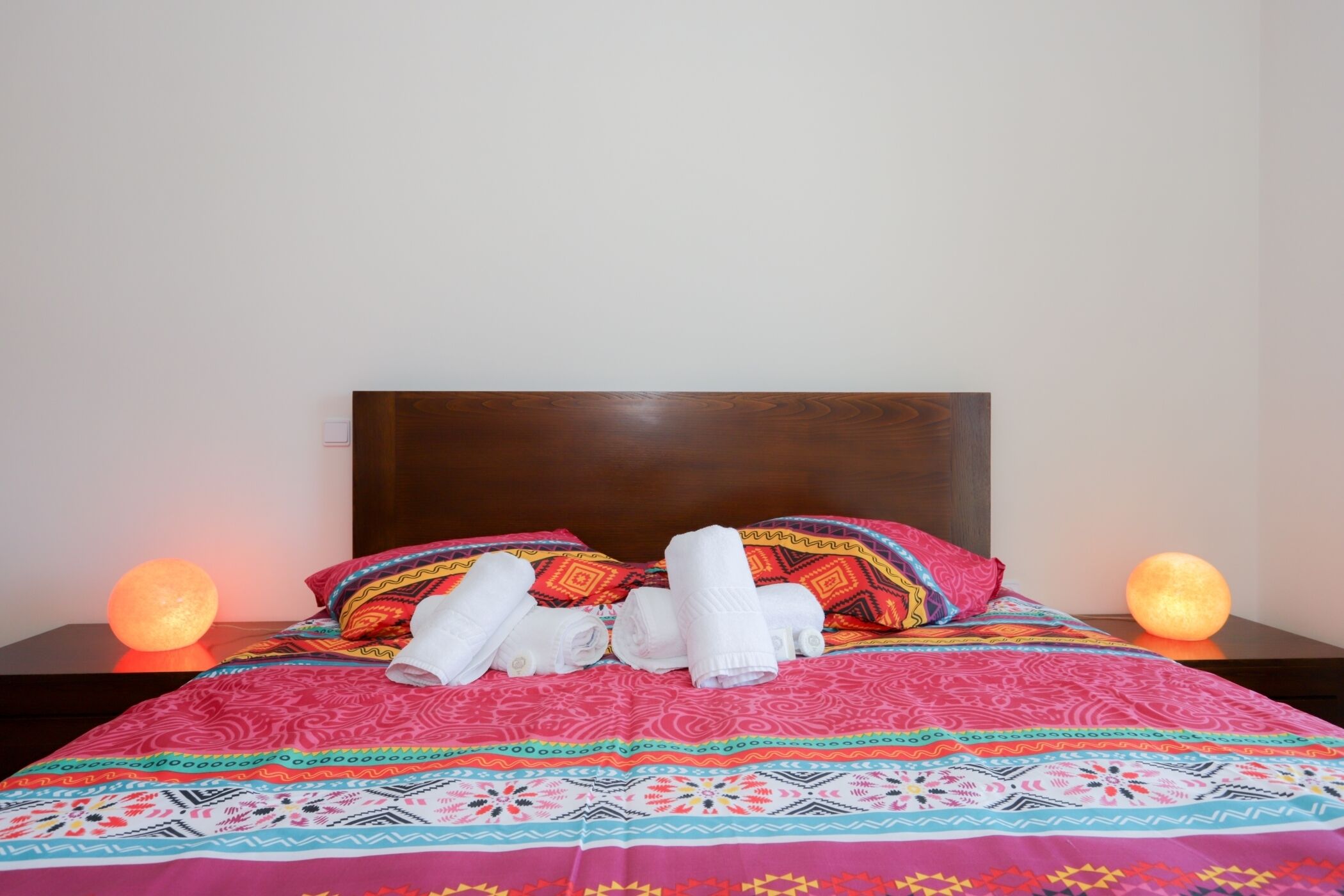 A bed with a colorful patterned bedspread, two pillows with a geometric design, and two round, glowing light sources on either side.