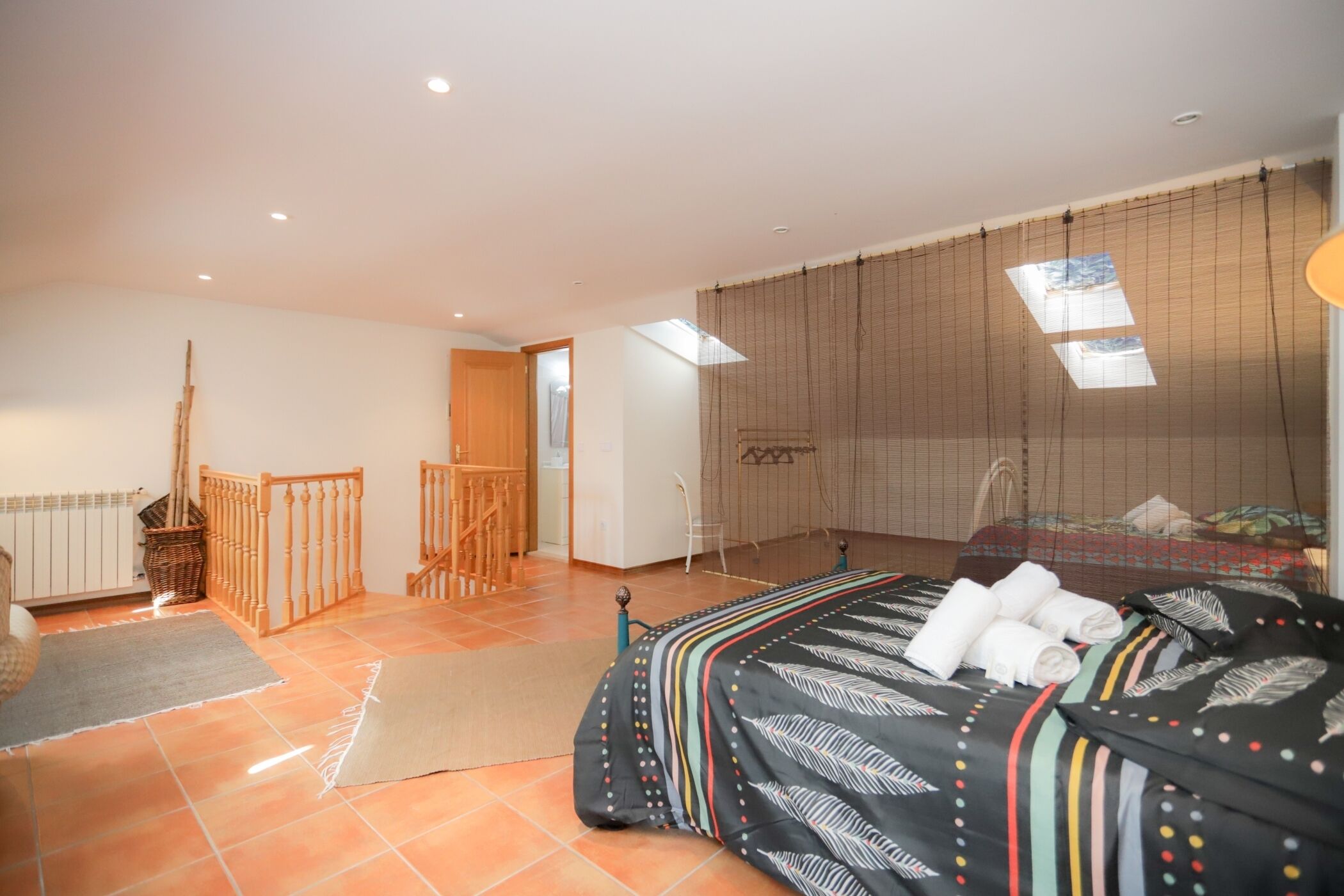 A bedroom with a bed, a window with blinds, a wooden chair, and a small balcony.