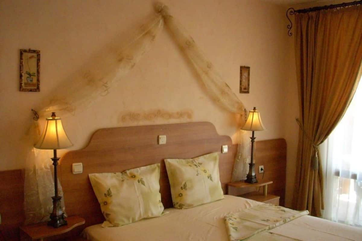 A hotel room with a wooden headboard, two bedside lamps, floral-patterned pillows, and a window with curtains.