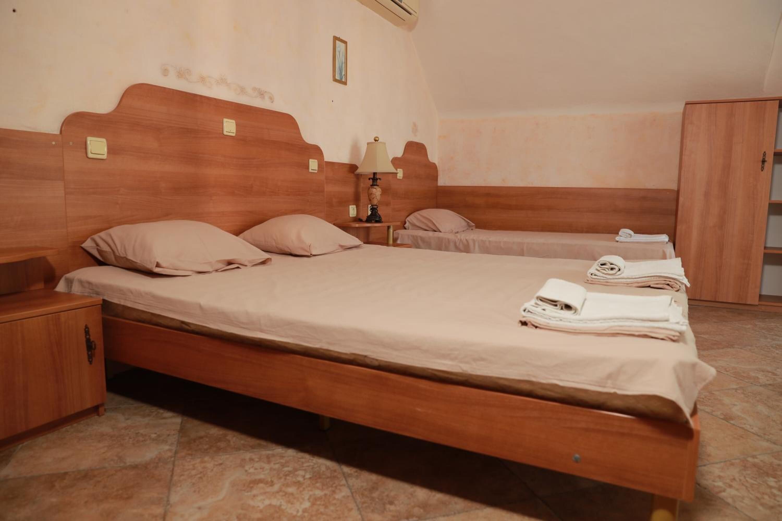 A bedroom with a large bed, a smaller bed, a nightstand, a lamp, and a wardrobe.