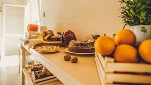 Un plan de travail de cuisine sur lequel sont disposés divers produits de boulangerie, notamment du pain, des viennoiseries et un gâteau, ainsi que des oranges fraîches et une plante en pot.
