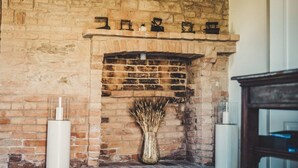 Une cheminée en briques ornée d’un vase contenant des plantes séchées, d’une bougie et d’un vase blanc posé sur le manteau de la cheminée.