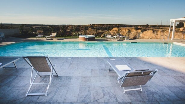 Une piscine dotée de chaises longues et d’un jacuzzi, entourée d’une terrasse carrelée et offrant une vue sur la campagne.