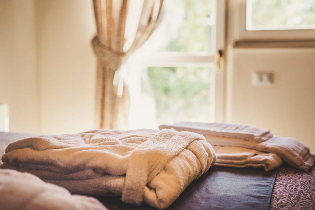 Un letto rifatto con coperta piegata e cuscini, una finestra con tende e un termostato a parete.