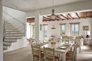A dining area with a table set for four, a staircase, and a view of the sea through windows.
