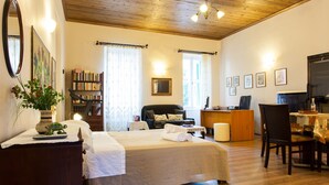 A hotel room with a bed, a desk, a chair, a bookshelf, and a dining table.