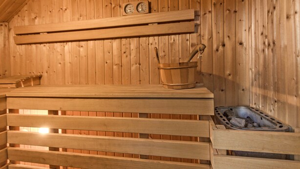 A wooden sauna with benches, a bucket, and a heater.