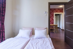 A hotel room with two beds, a wooden floor, a dining area with a table and chairs, and a red patterned wall.