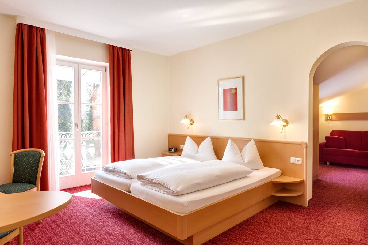 Quarto de hotel com cama, cadeira, escrivaninha e sofá vermelho.