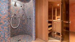 A modern bathroom with a mosaic tile shower wall, wooden sauna benches, and a glass-enclosed sauna area.