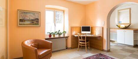 Een gezellige kamer met een leren fauteuil, een bureau met een computer, een radiator en een raam met planten.