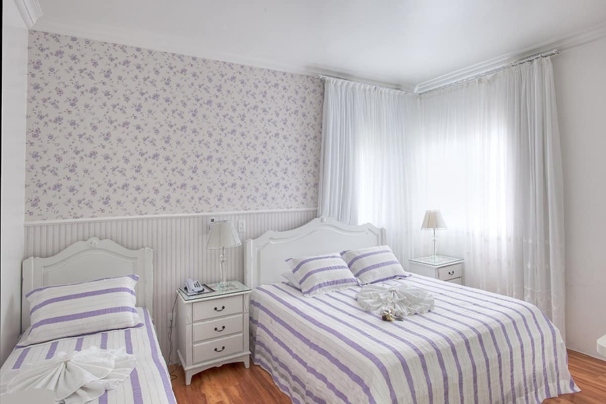 A bedroom with two beds, a nightstand, a lamp, and a window with curtains.