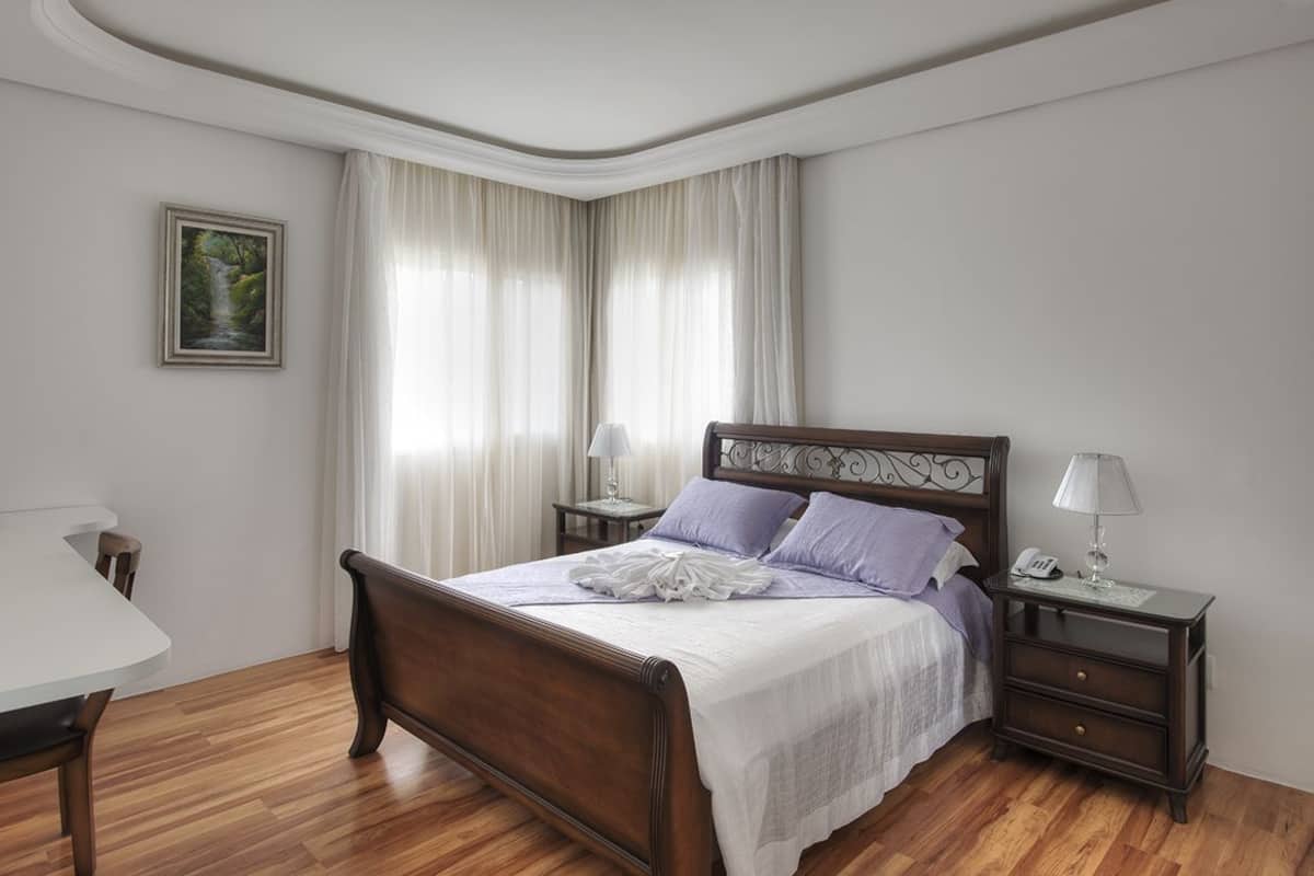 A bedroom with a wooden bed, a bedside table with a lamp, a nightstand with a phone, and a painting on the wall.