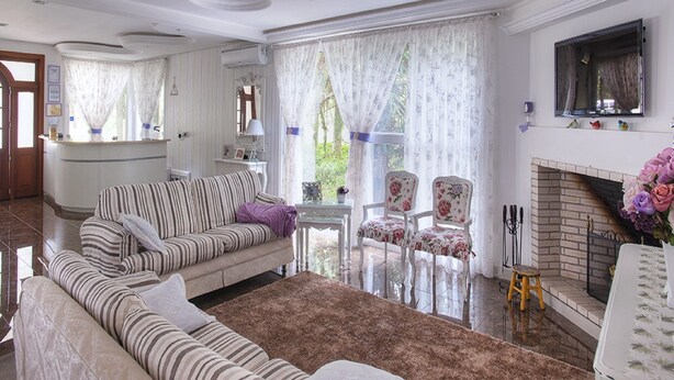 A living room with a sofa, armchairs, a fireplace, and a view of greenery outside. - Pousada Perfume de Canela (Canela)