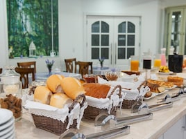 A breakfast buffet with various breads and pastries, a coffee station, and a juice bar.