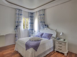 Quarto com cama, mesas de cabeceira e janela com cortinas.