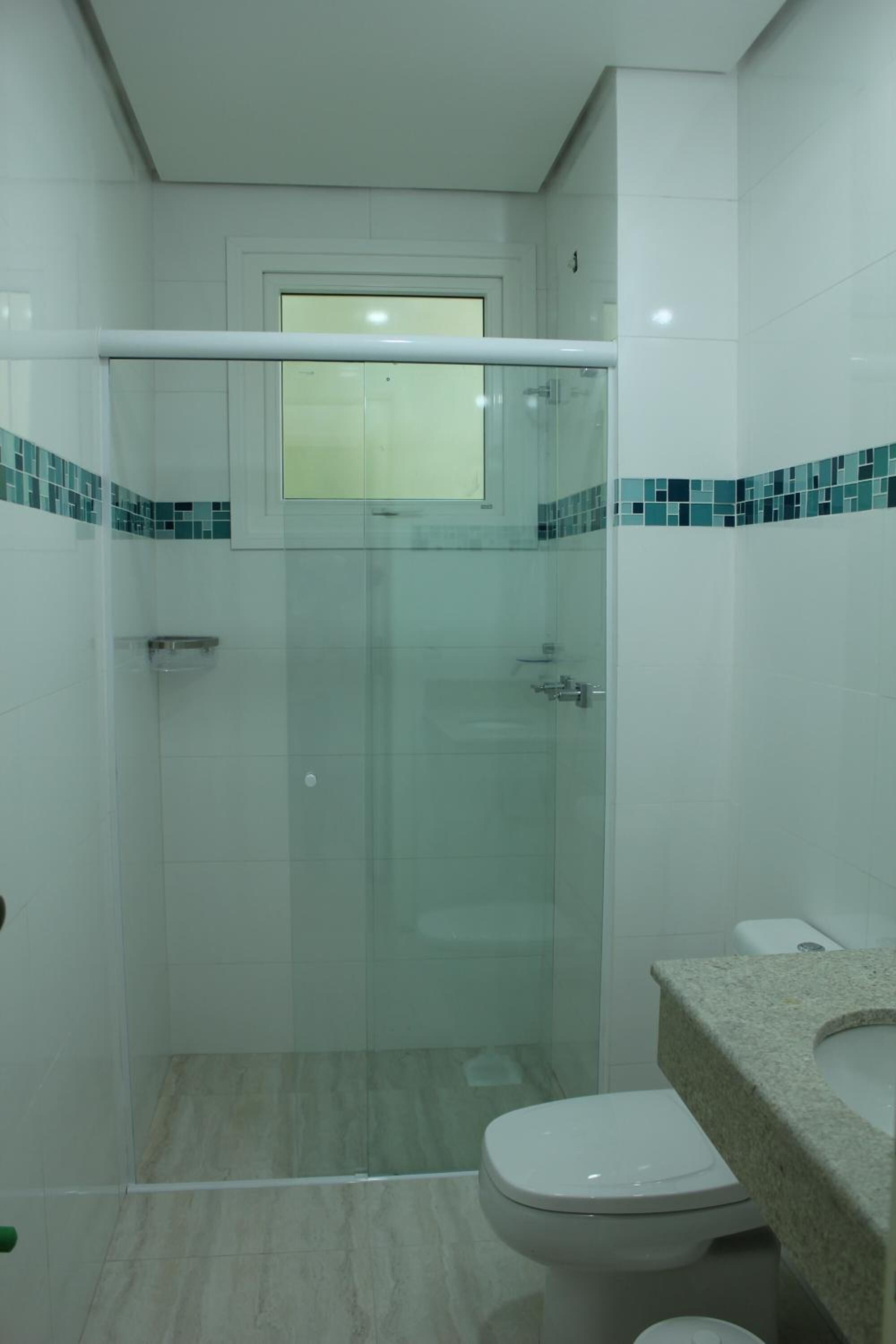Een badkamer met een douchecabine met glazen wanden, een toilet en een wastafel met een granieten aanrechtblad.