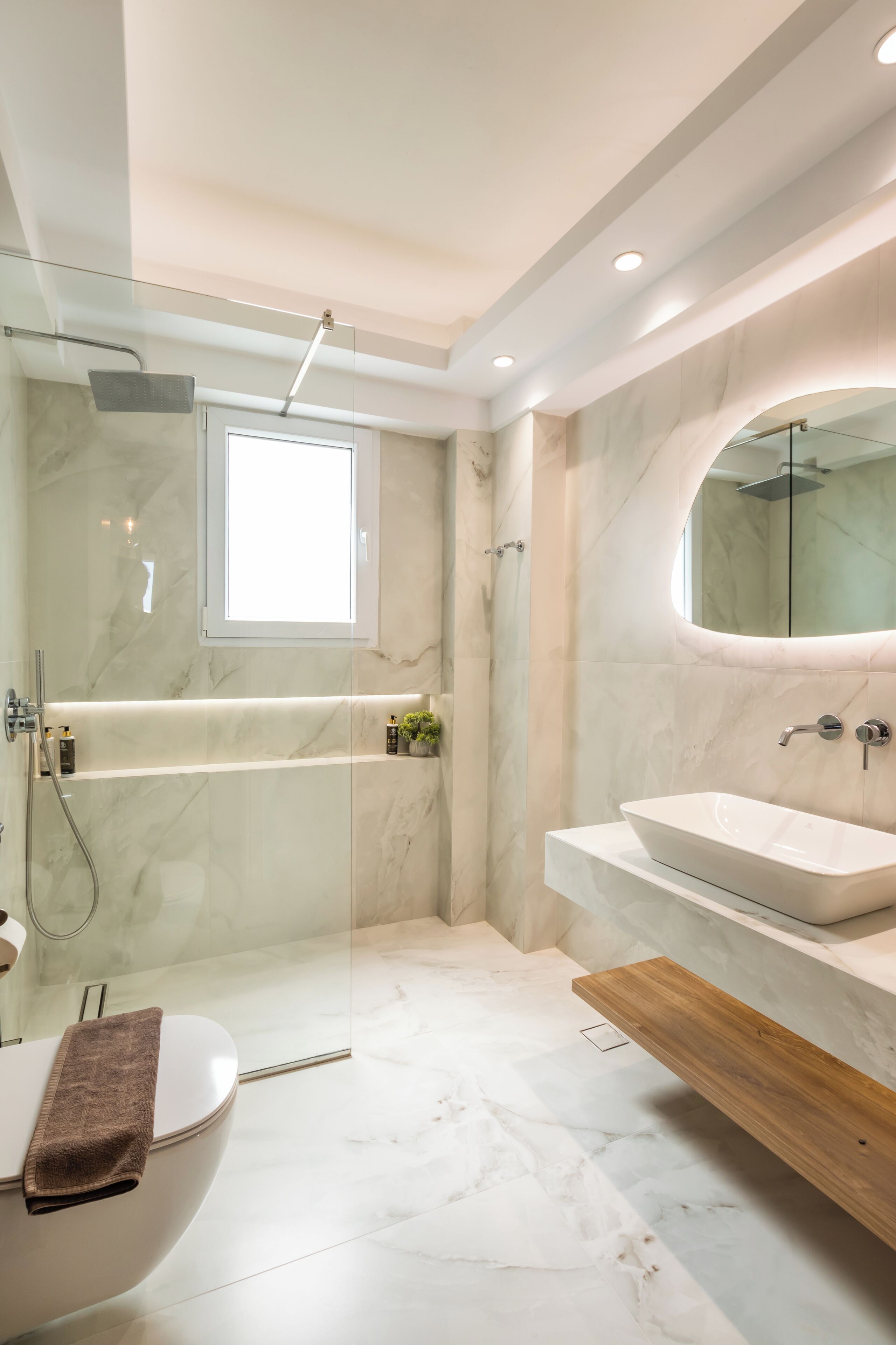 Een moderne badkamer met een douche met glazen wand, een vrijstaand bad, een witte wastafel en een houten badkamerkast.