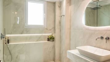 Een moderne badkamer met een douche met glazen wand, een vrijstaand bad, een witte wastafel en een houten badkamerkast.