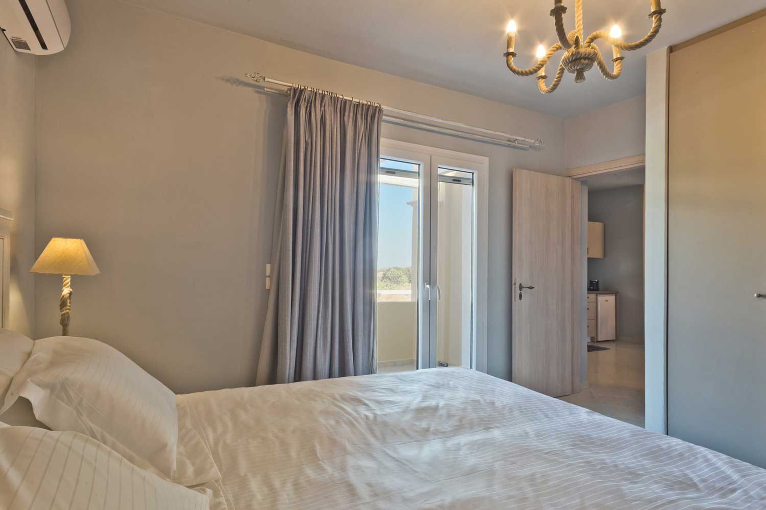 A bedroom with a bed, a lamp, a chandelier, and a sliding door leading to a balcony.