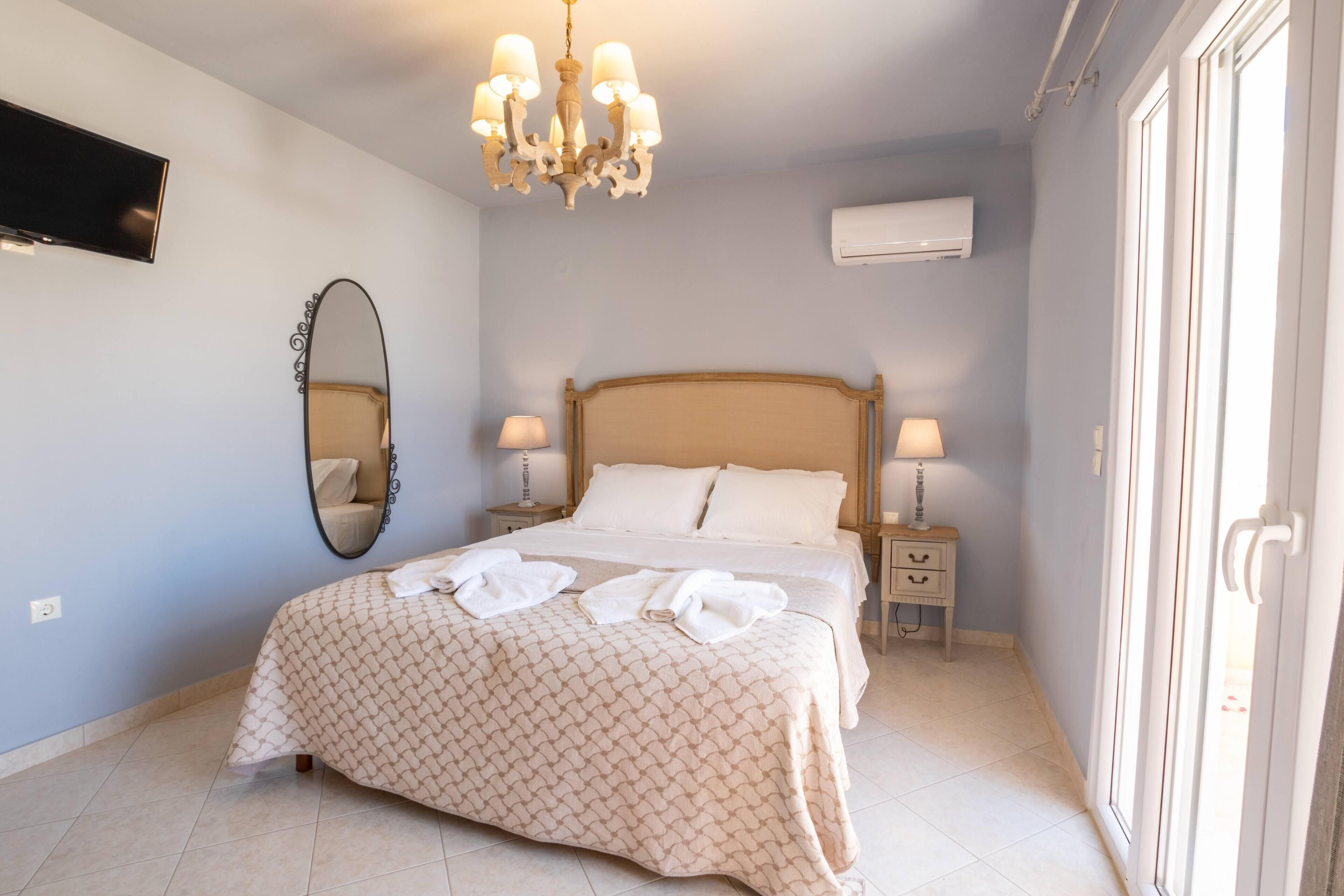 A bedroom with a bed, bedside lamps, a mirror, a chandelier, and an air conditioning unit.