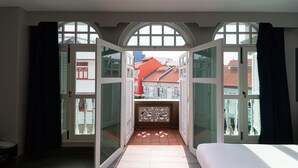 Un dormitorio con una cama grande, vistas a través de puertas abiertas de un espacio exterior con suelo de baldosas, y un balcón con barandilla.