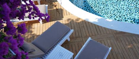 A wooden deck with lounge chairs and a pool.