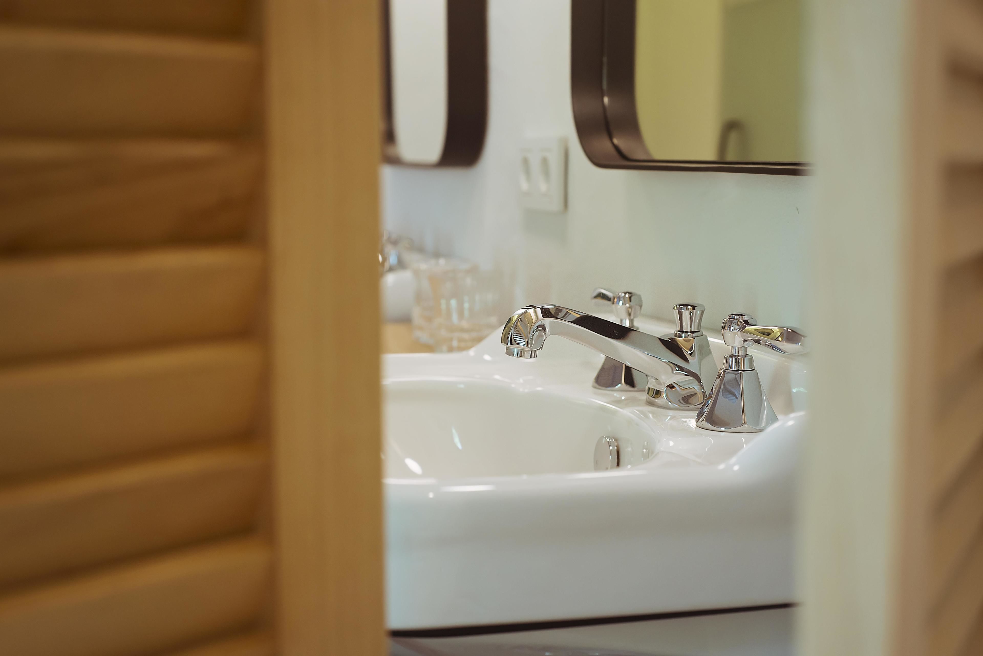 Ein Badezimmer mit einem weißen Waschbecken, zwei Wasserhähnen und einem Spiegel.