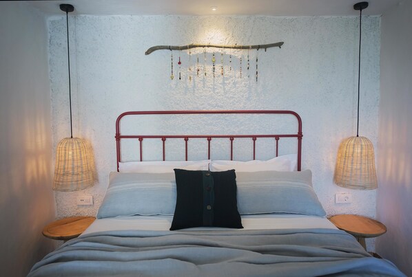 Una cama con cabecera de metal roja, dos mesitas de noche y lámparas colgantes.