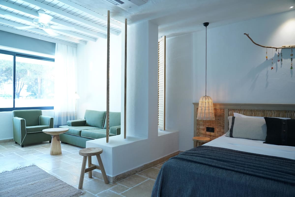 A modern bedroom with a large bed, a hanging light fixture, and a view of the outdoors.