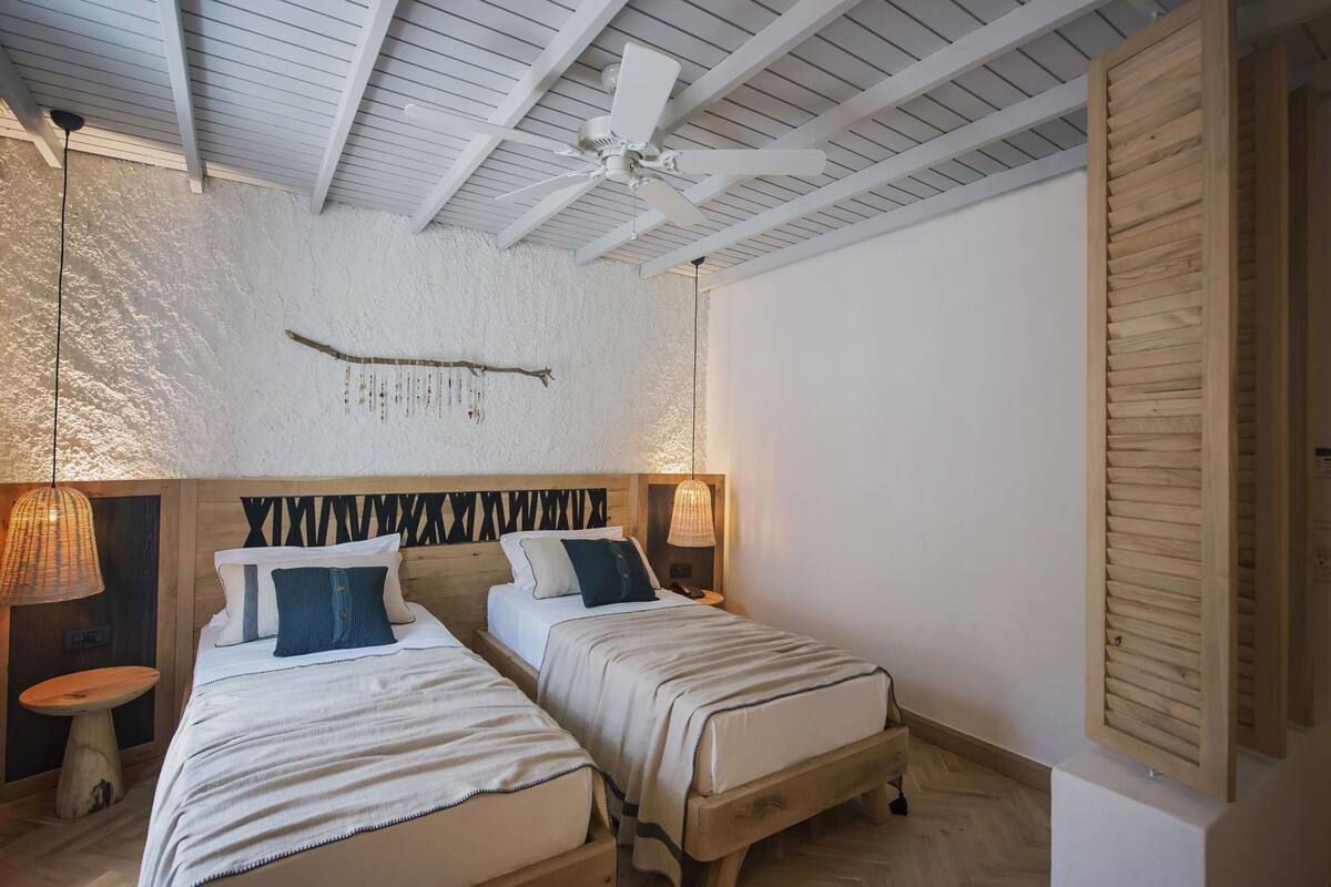 A bedroom with two beds, a ceiling fan, a wall-mounted light fixture, and a wooden door.