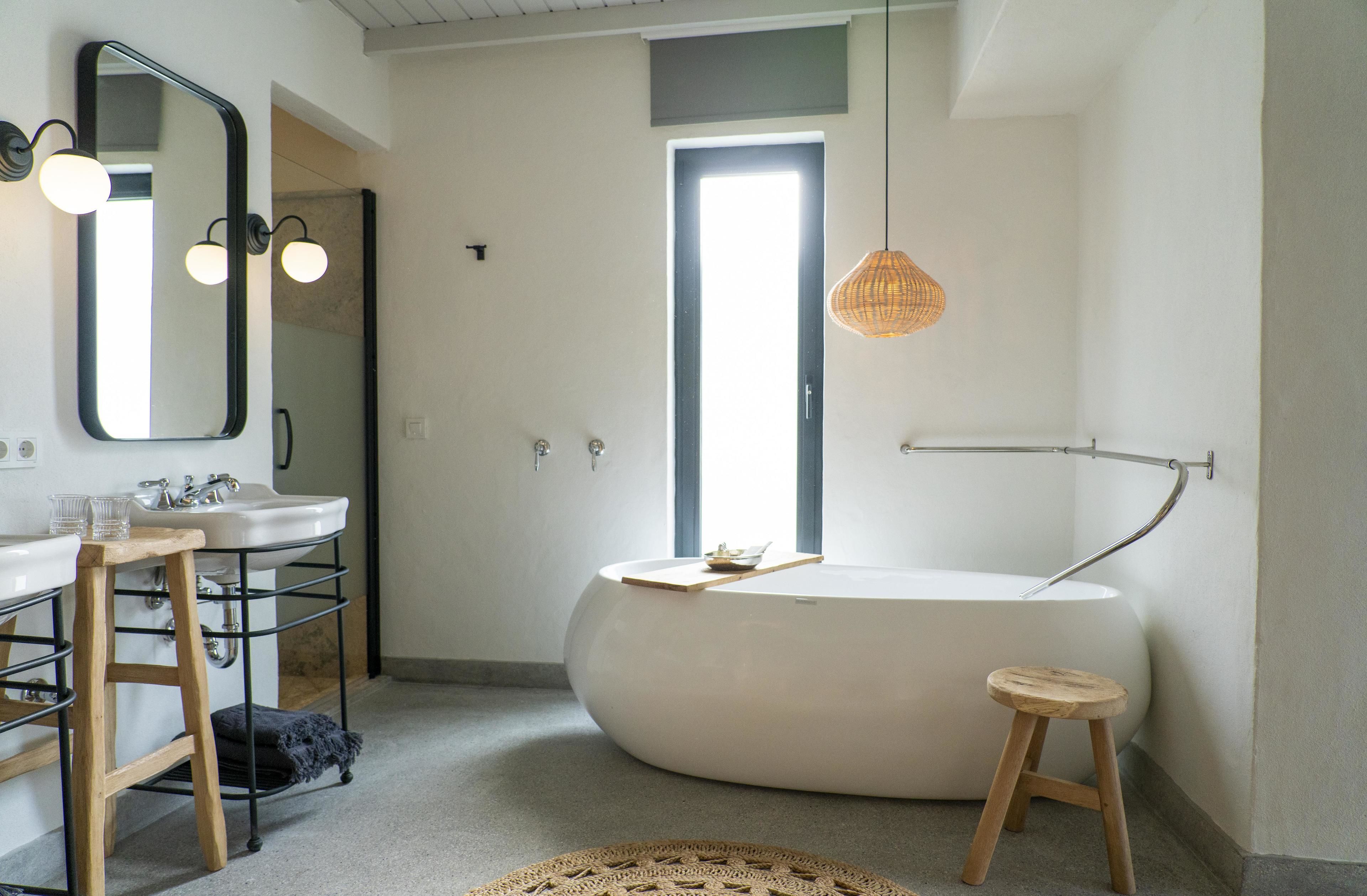 A modern bathroom with a freestanding bathtub, a large mirror, and a stool.
