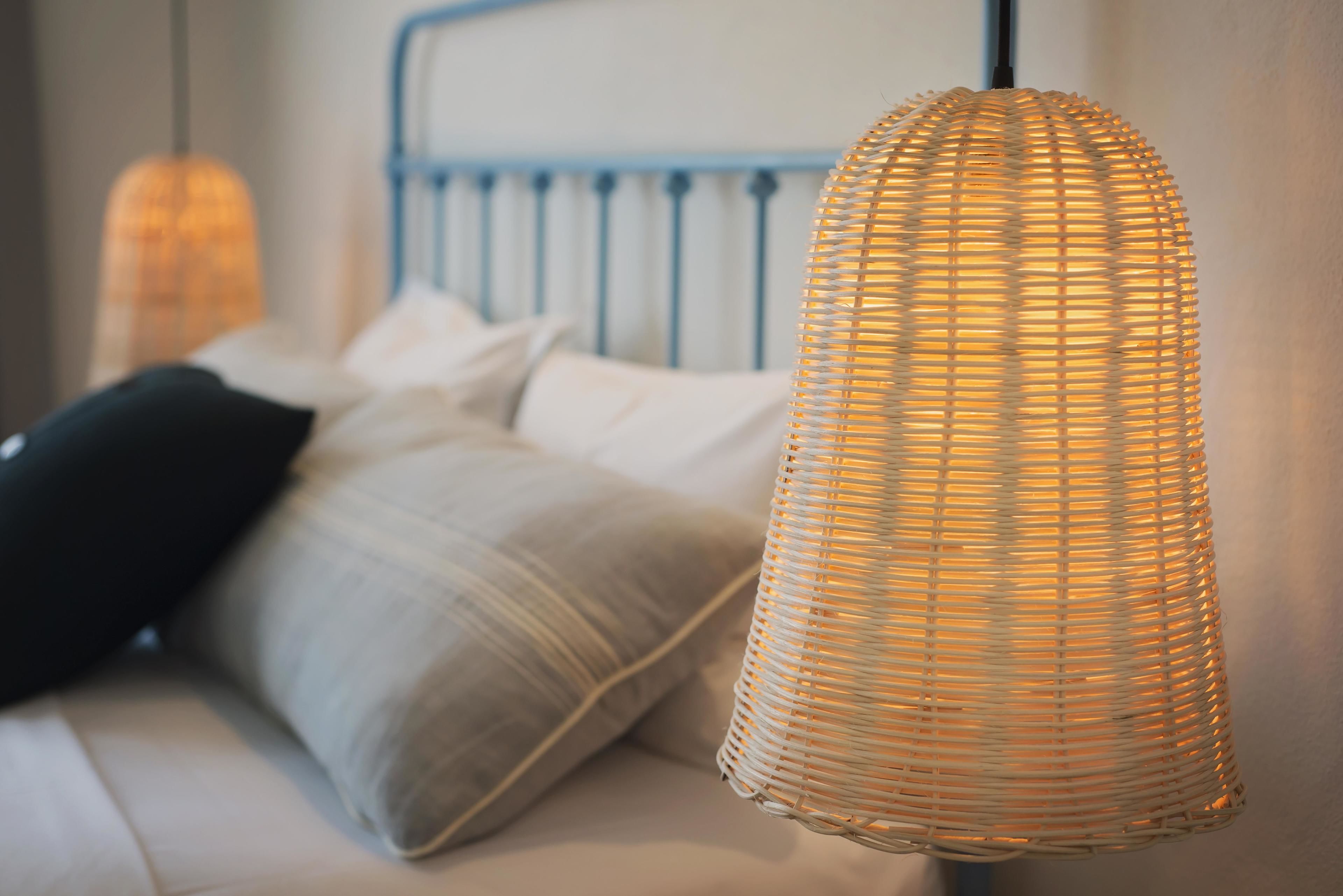 A wicker pendant light hanging over a bed with a blue headboard and white bedding.