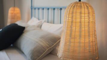 A wicker pendant light hanging over a bed with a blue headboard and white bedding.