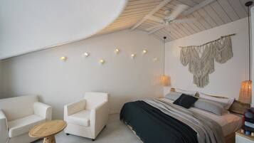Un dormitorio moderno con cama, dos sillas blancas, una mesita de madera y un tapiz de macramé en la pared.