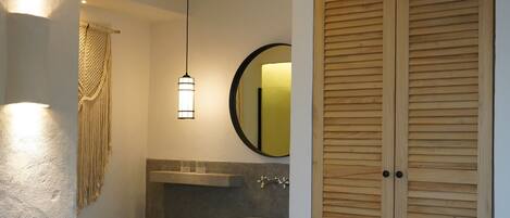 A bathroom with a wooden vanity, a round mirror, a hanging light fixture, and a wooden stool.