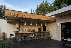 Zona de bar con un letrero de madera que dice 'MANDALA', paredes de piedra y lámparas colgantes.