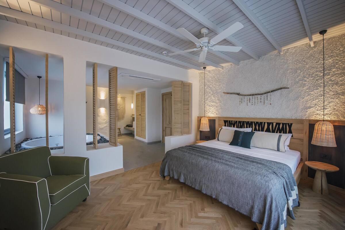 A modern bedroom with a large bed, a ceiling fan, and a stone wall.