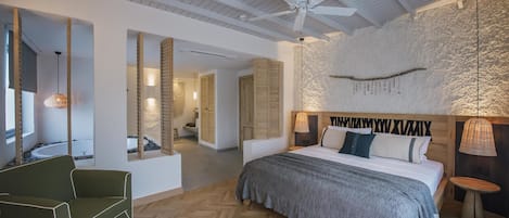 A modern bedroom with a large bed, a ceiling fan, and a stone wall.