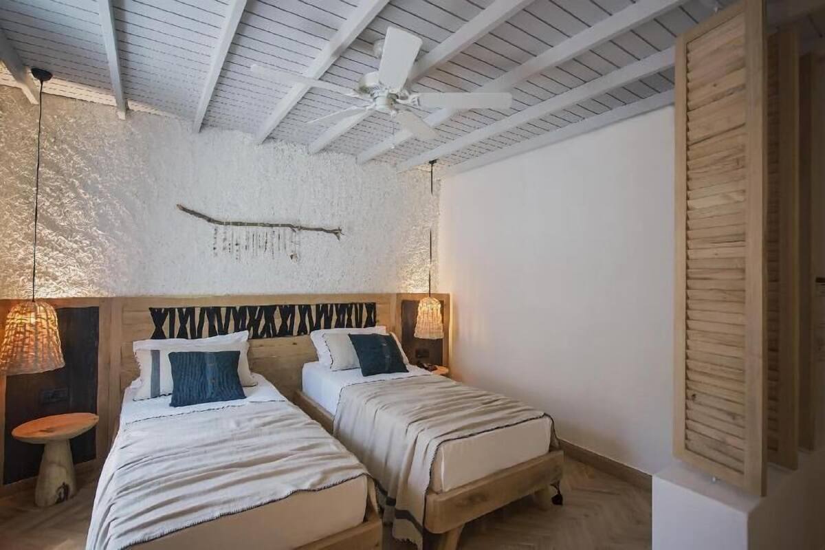 A room with two beds, a ceiling fan, and a rustic wall texture.