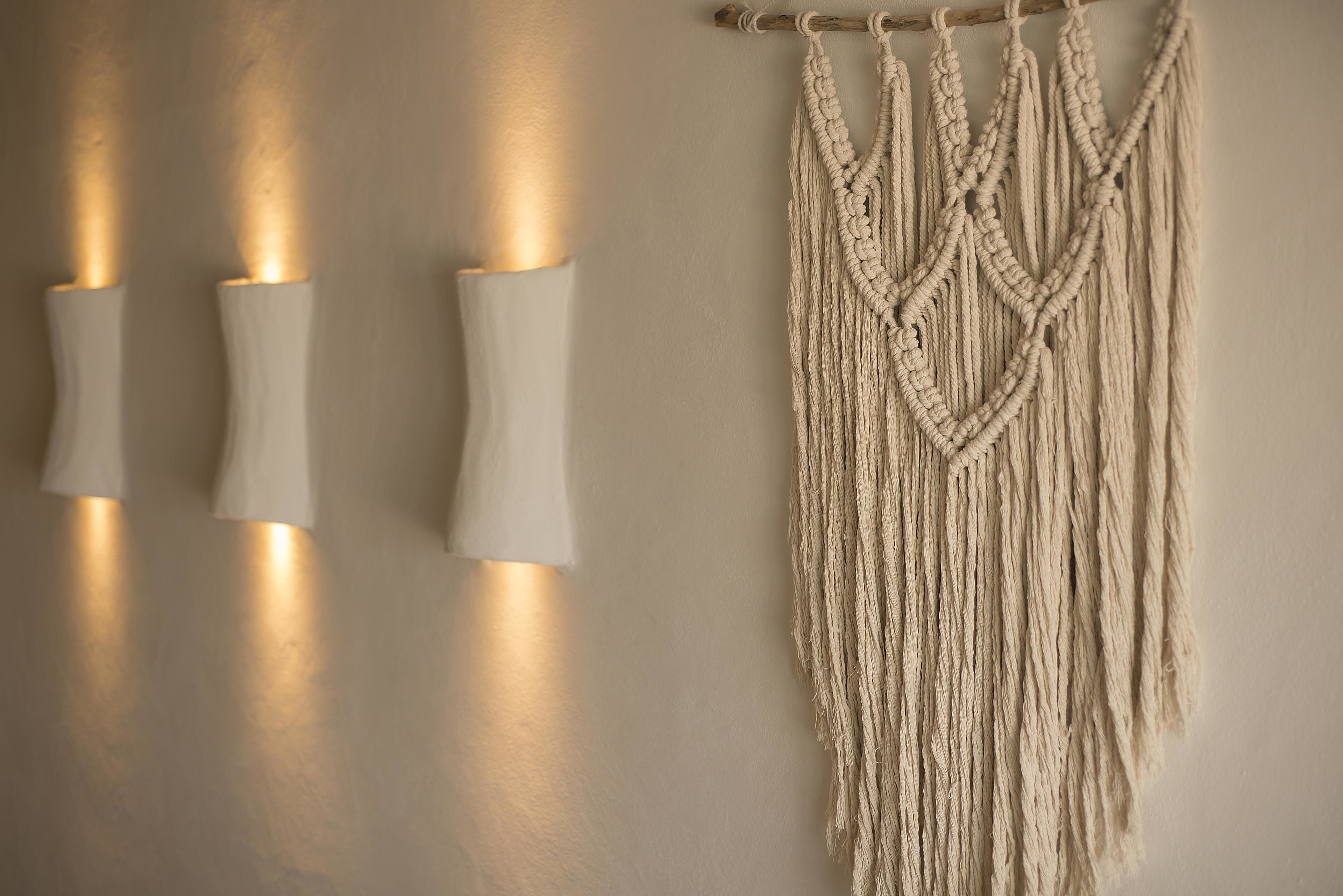 A wall with three wall-mounted light fixtures and a macramé wall hanging.