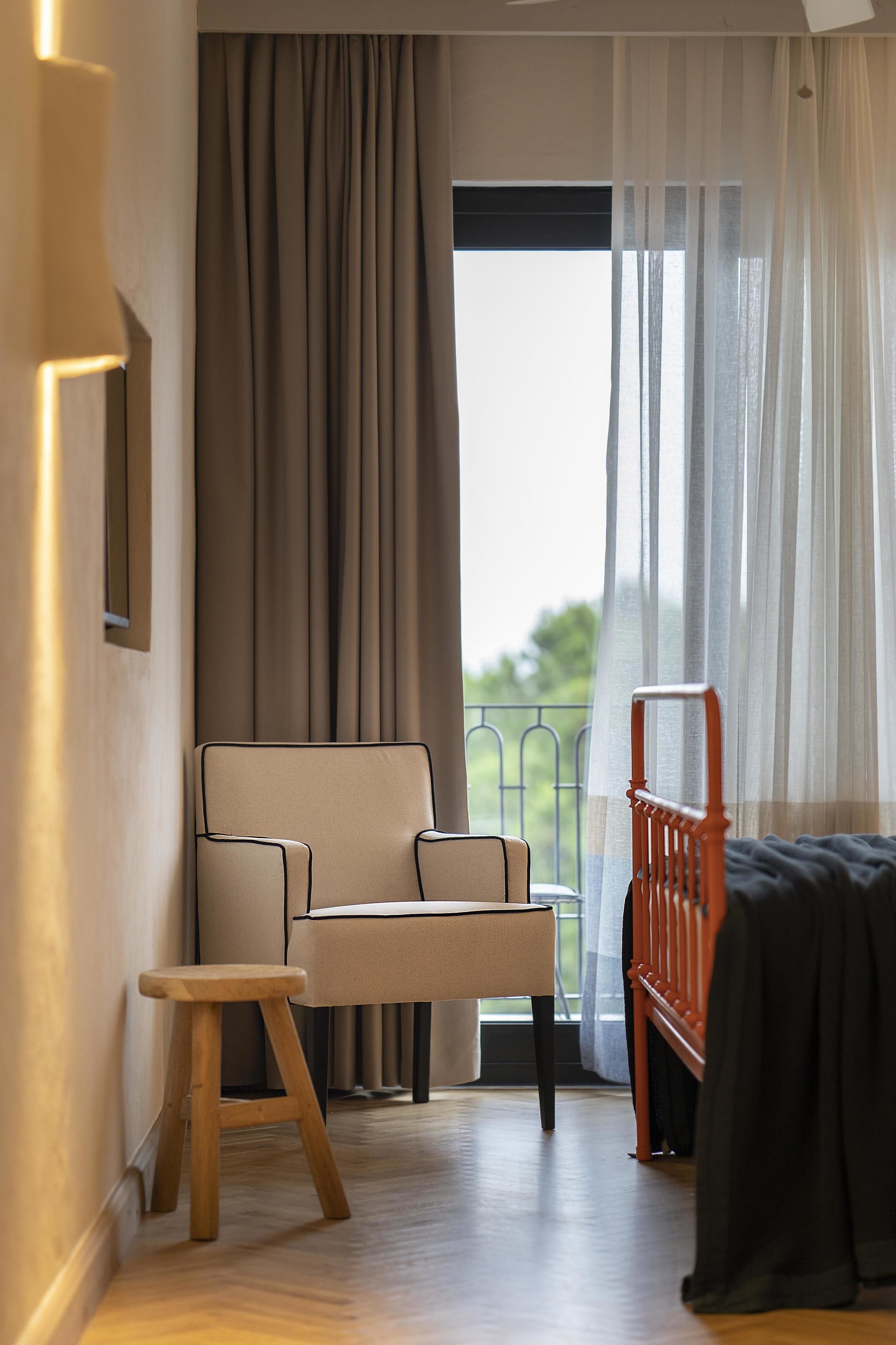 A room with a sofa, a small stool, a bed, and a balcony with curtains.